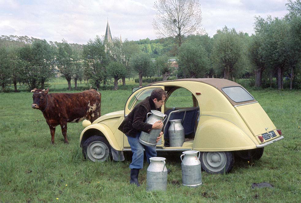 un agricoltore mentre carica contenitori di latte nella 2 cavalli del '60